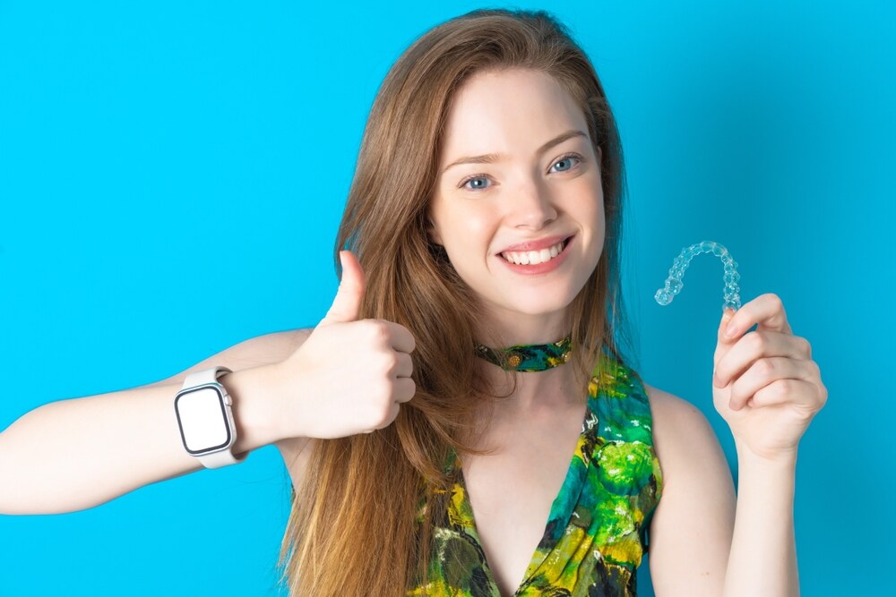 Person gently adjusting clear Invisalign aligners with a smile